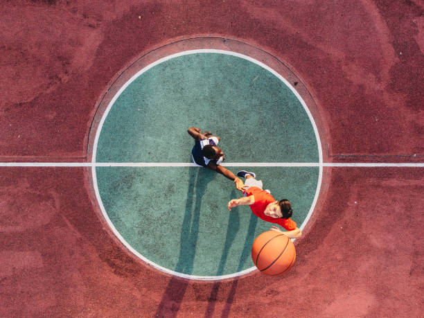 Two friends are jumping to take a basketball ball on the center field Two friends are jumping to take a basketball ball on the center field. Aerial point of view. basketball player photos stock pictures, royalty-free photos & images