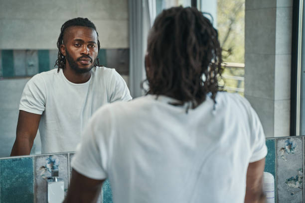 Calm male concentrated on examining his face in bathroom Waist-up portrait of serious focused man looking at his reflection in wall-mounted mirror looking stock pictures, royalty-free photos & images