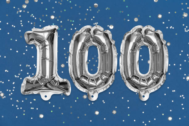 istock Silver foil balloon number, digit one hundred on a blue background with sequins. Birthday greeting card 1354176351