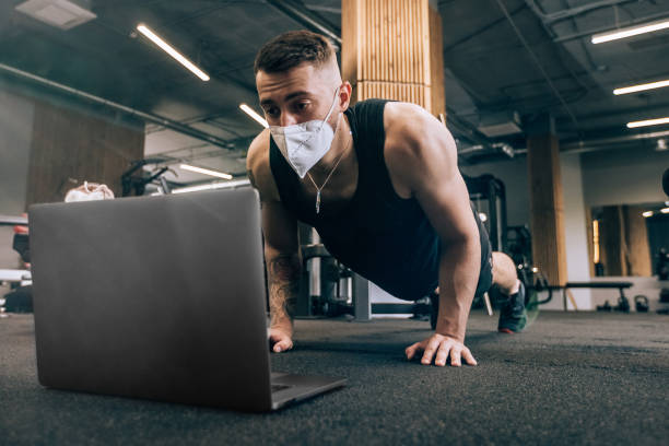 istock Sports person teaching and learning online lessons on laptop at the gym. Man using computer for live-streaming, video call and fitness conference Portrait with face mask in lockdown of coronavirus 1354176447