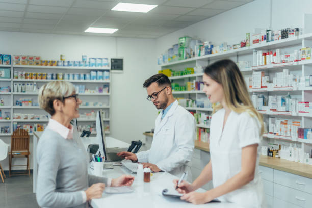 istock Male pharmacist working on a computer while female pharmacist is giving prescription medications to senior patient 1354176617