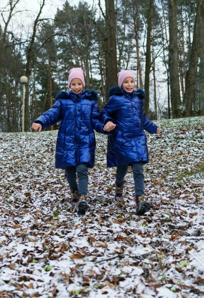 две девочки-близнеца бегут вниз по склону, покрытого первым снегом - twin falls стоковые фото и изображения