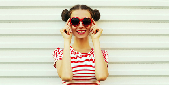 Portrait of cheerful smiling young woman wearing a red heart shaped sunglasses striped t-shirt with cool hairstyle on white background