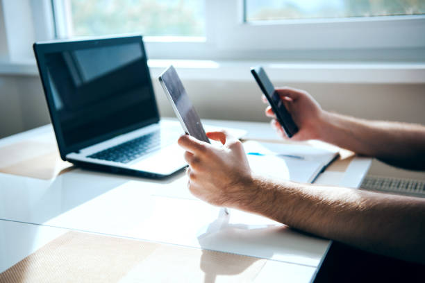 istock Man's hands holding two phones and a laptop on the table. Modern technology. Transmitting information from one device to another 1354177976