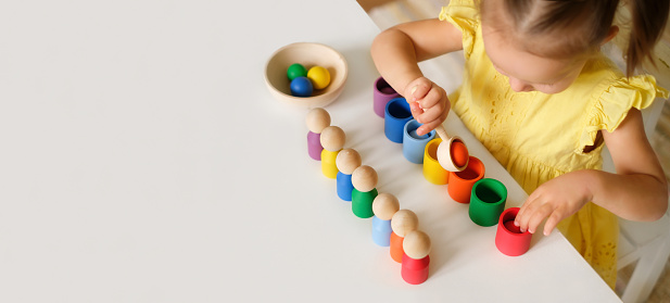 Kid plays with an educational toy that helps to learn colors at the kindergarten table. A banner with copy space. Preschool Children's Development School. Fine motor skills of hands.