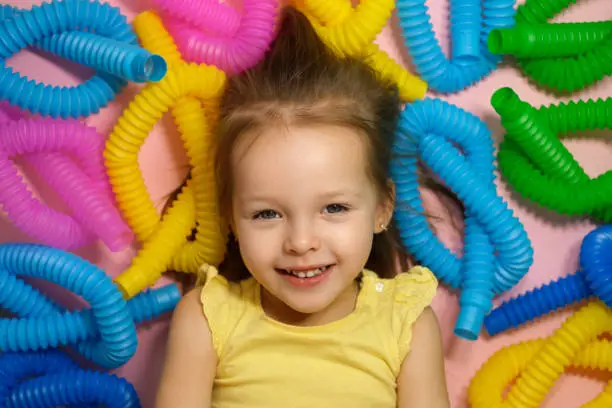 Photo of Two-year-old girl surrounded by trendy bright colorful pop tubes toys.