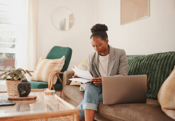 istock Shot of a young woman using a laptop while going through paperwork at home 1354178805