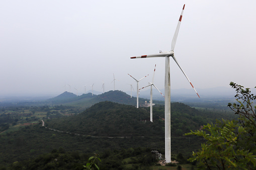 A High angle picture of Modern Windmill on a Hill range used for power generation and transmission in Hassan countryside in Karnataka, India.