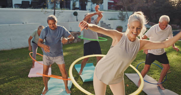 aufnahme einer gruppe von senioren, die mit hoola hoops trainieren - yoga exercising outdoors group of people stock-fotos und bilder