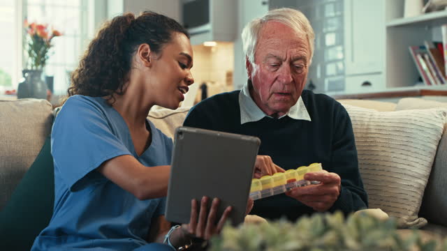 4k video footage of a female nurse using a digital tablet while showing her senior patient his pill box
