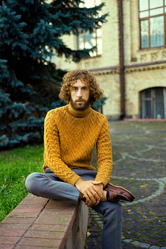 Portrait of  young Caucasian man with curly hair in mustard yellow sweater near university