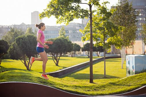 Young woman jogging on dedicated running track with grass surface, staying active and healthy in the city