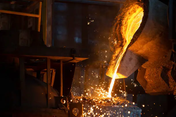 Pouring liquid molten metal from transport vessel to casting mould using forklift in steel mill.