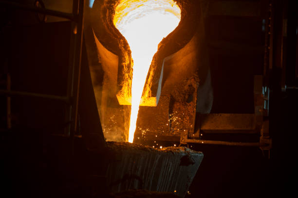 Pouring liquid molten metal from transport vessel to casting mould using forklift in steel mill.