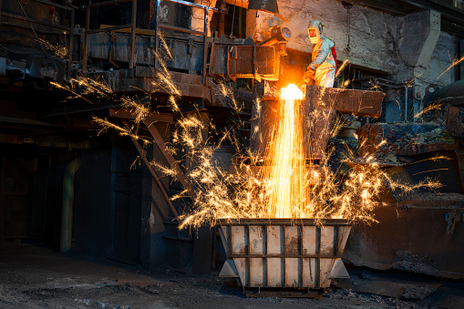 Male foundry worker creating sparks pouring molten metal in the container.