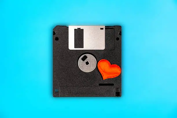 Floppy Disk Drive with a Red Heart on the Blue Paper Background closeup