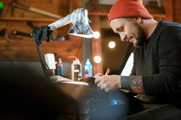 istock Professional male bearded caucasian tattoo master is working in cozy atmospheric studio 1354192541