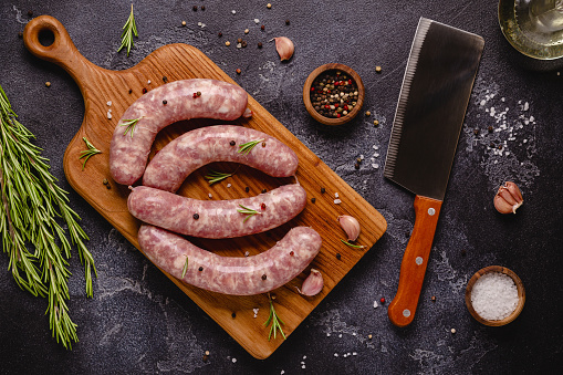 Raw sausages and ingredients for cooking on a black stone table, top view.