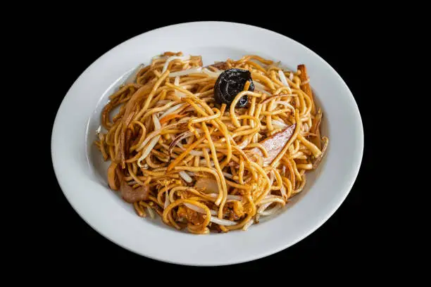 Photo of Asian Chow Mein noodles with chicken and vegetables and mushrooms, in a white plate. A popular oriental dish. On a black background.