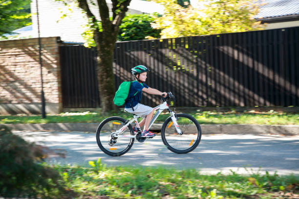 Boy on his bike in suburbs Boy with cycling helmet going to school on his bike, riding through suburb. With backpack ready for scool. bicycle cycling school child stock pictures, royalty-free photos & images