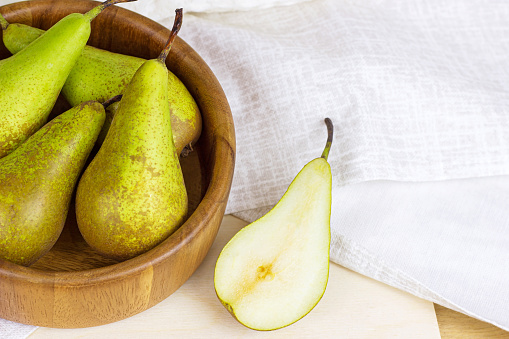 Fresh green organic pears ripe in the round wooden bowl on light background in the kitchen.