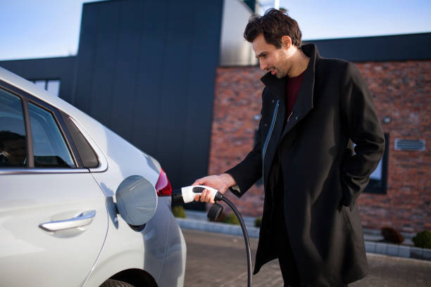 Young man on a parking lot, charging his electric car Photo of a young man on a parking lot, charging his electric car plugging in photos stock pictures, royalty-free photos & images