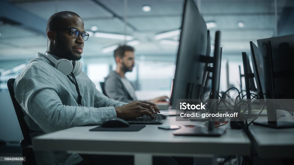 Diverse Office: Black IT Programmer Working on Desktop Computer. Male Specialist Creating Innovative Software Engineer Developing App, Program, Video Game. Terminal with Coding Language. Computer Stock Photo