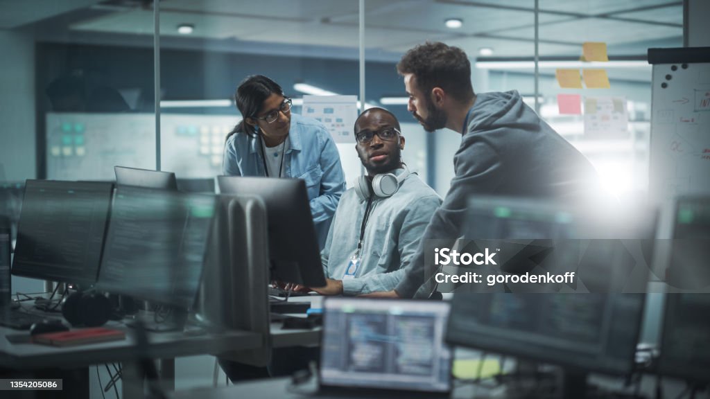 Diverse Group of Professionals Meeting in Modern Office: Brainstorming IT Programmers Use Computer Together, Talk Strategy, Discuss Planning. Software Engineers Develop Inspirational App Program Technology Stock Photo