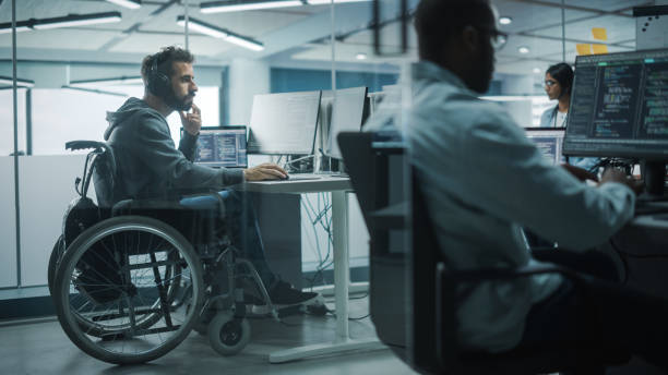 istock Disability-Friendly Office: Amazing IT Programmer with Disability in a Wheelchair Working on Desktop Computer. Male Specialist Create Inspirational Software. Engineer Develop Innovative App, Program 1354205141