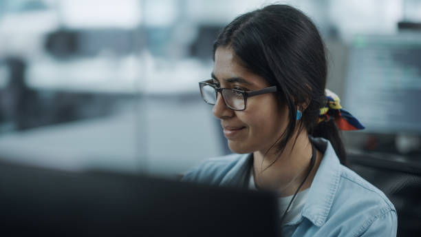 istock Diverse Office: Portrait of Beautiful Indian IT Programmer Working on Desktop Computer. Female Specialist Wearing Glasses Create Innovative Software. Professional Engineer Develop Inspirational App 1354205196
