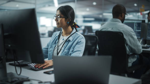 istock Diverse Office: Portrait of Talented Indian Girl IT Programmer Working on Desktop Computer in Friendly Multi-Ethnic Environment. Female Software Engineer Wearing Glasses Develop Inspirational App 1354205260