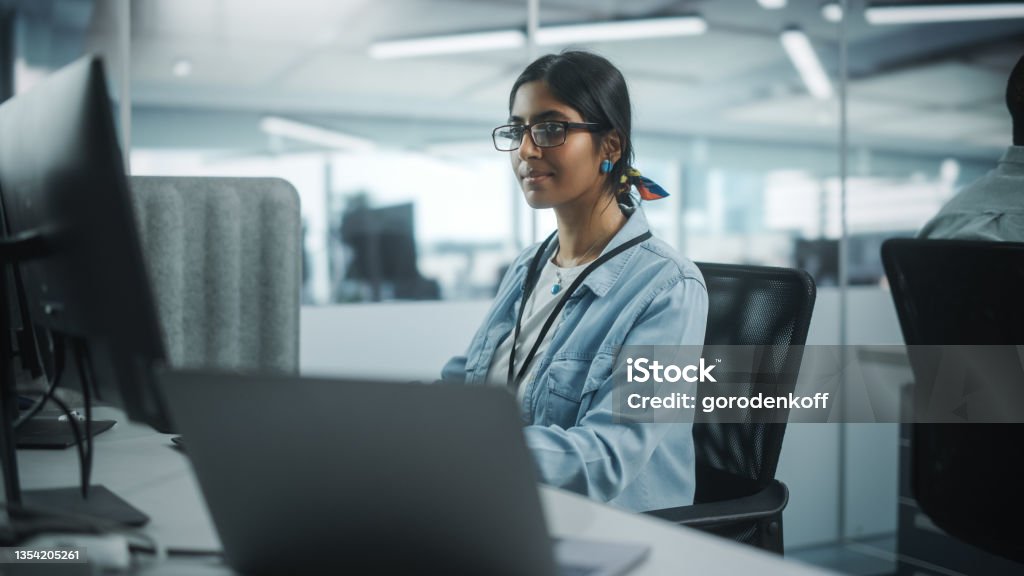 Diverse Office: Portrait of Talented Indian Girl IT Programmer Working on Desktop Computer in Friendly Multi-Ethnic Environment. Female Software Engineer Wearing Glasses Develop Inspirational App Computer Programmer Stock Photo
