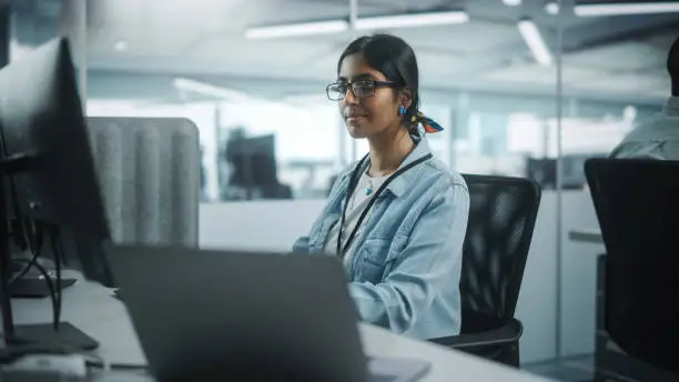 Photo of Diverse Office: Portrait of Talented Indian Girl IT Programmer Working on Desktop Computer in Friendly Multi-Ethnic Environment. Female Software Engineer Wearing Glasses Develop Inspirational App