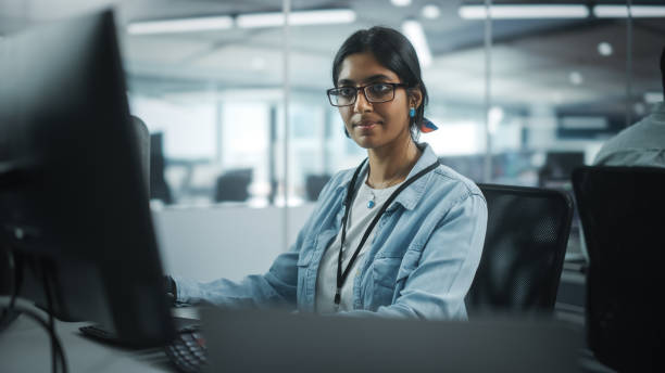 istock Diverse Office: Portrait of Talented Indian Girl IT Programmer Working on Desktop Computer in Friendly Multi-Ethnic Environment. Female Software Engineer Wearing Glasses Develop Inspirational App 1354205279