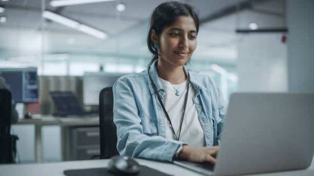 istock Diverse Office: Portrait of Beautiful Smiling Indian IT Programmer Working on Desktop Computer. Female Specialist Creating Innovative Software. Professional Engineer Develop Inspirational App 1354205459