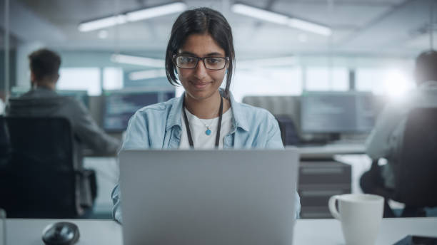 istock Diverse Office: Portrait of Smiling Indian IT Programmer Working on Desktop Computer. Female Specialist Create Innovative Software. Professional Engineer Develop App. 1354205477