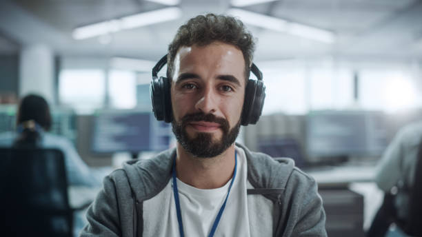 istock Office: Portrait of Happy IT Programmer Wearing Headphones Working on Desktop Computer. Male Software Engineer Developing App, Video Game. Listening to Podcast, Music 1354205488