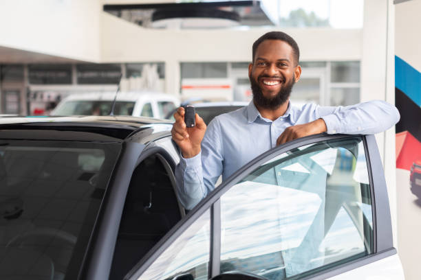 salon samochodowy. czarny mężczyzna pozujący w pobliżu nowego samochodu z kluczykami w ręku - car african descent shopping car dealership zdjęcia i obrazy z banku zdjęć