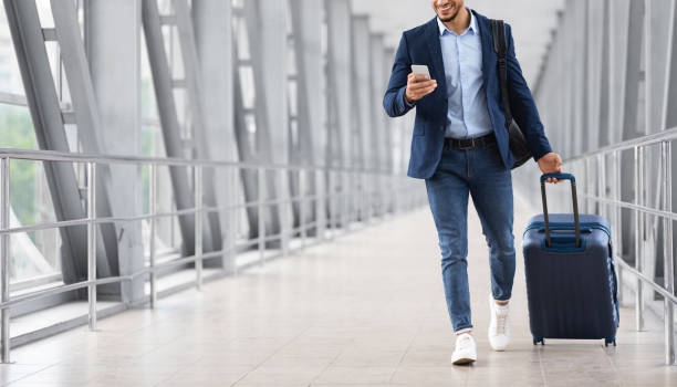 istock Unrecognizable Young Businessman Using Smartphone While Walking With Suitcase In Airport 1354206625