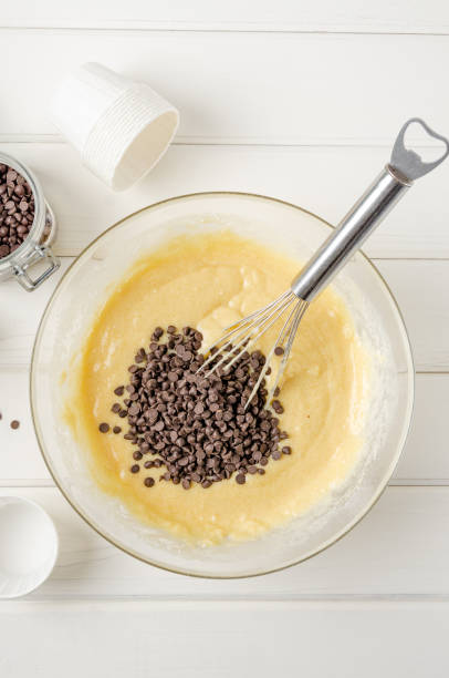 istock Muffin dough with chocolate chips in a bowl on a white wooden background. Recipe step by step. 1354206836