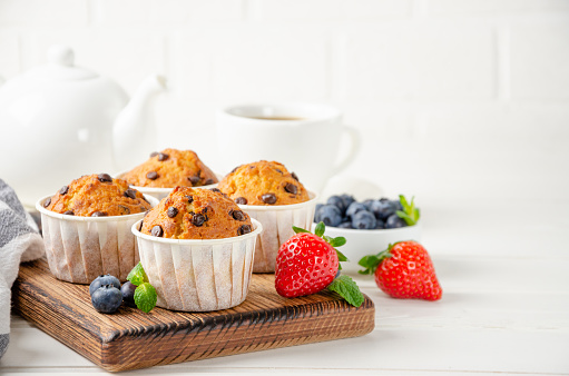 Muffins with chocolate chips on a wooden bord on a white background with fresh berries. Copy space