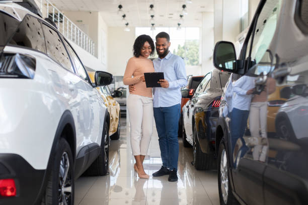 giovane coppia nera che sceglie l'auto nel moderno centro di concessionaria, controllando le caratteristiche del veicolo - car african descent shopping car dealership foto e immagini stock