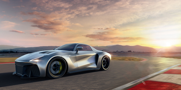 Side view of a generic silver sports car moving at high speed close to the camera. The roadster is driving on a racetrack at high speed causing motion blur in the foreground. The action takes place at dawn. With selective focus on the foreground.