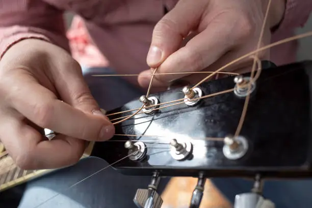 Photo of Hands male inserts new strings in an acoustic guitar. Repair of musical instruments.