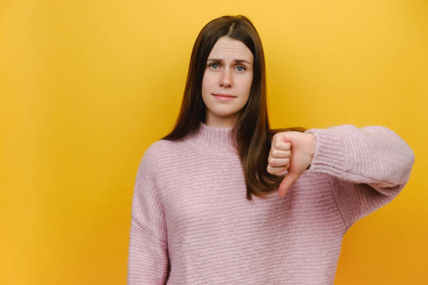 istock Young serious strict disappointed millennial woman show thumb down dislike gesture refusing say no, wearing pink knitted sweater, isolated on yellow color background studio. People lifestyle concept 1354210663