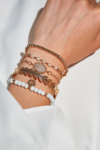 Cropped close-up shot of a female wrist with a golden ethnic bracelets set with various decorative embellishments. The lady is dressed in a white shirt. The photo is made on the white background.