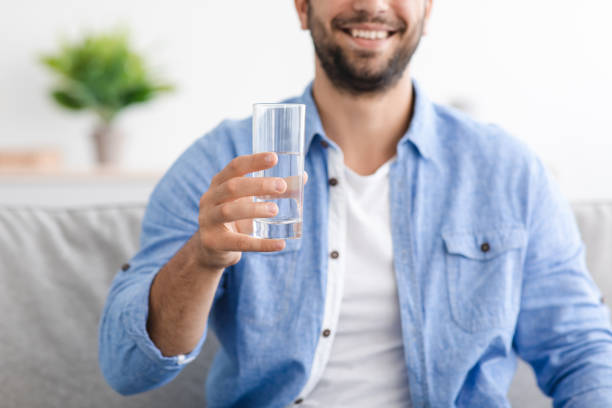 istock Smiling middle aged caucasian guy with beard sits on sofa and holds glass with clean still water 1354211354
