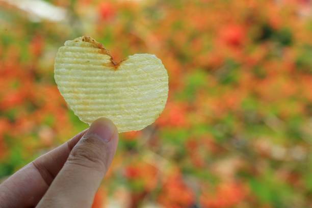 patatina a forma di cuore in mano di donna con foglie colorate in sfondo autunnale. - potato chip foto e immagini stock