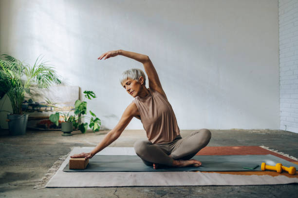 senior-frau macht home workout training - floor women sitting yoga stock-fotos und bilder