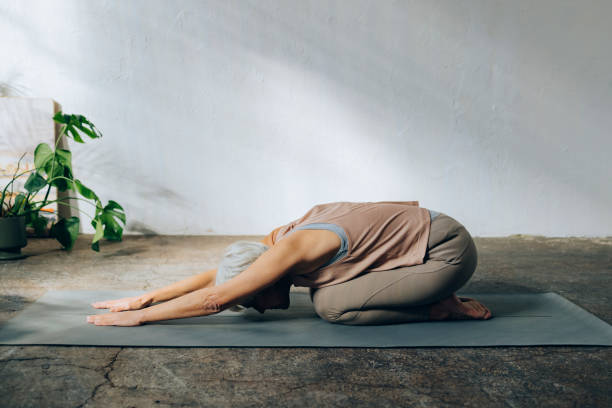 An Anonymous Senior Woman Practicing Yoga at Home Unrecognizable female relaxing after training on a gray exercise mat. childs pose stock pictures, royalty-free photos & images